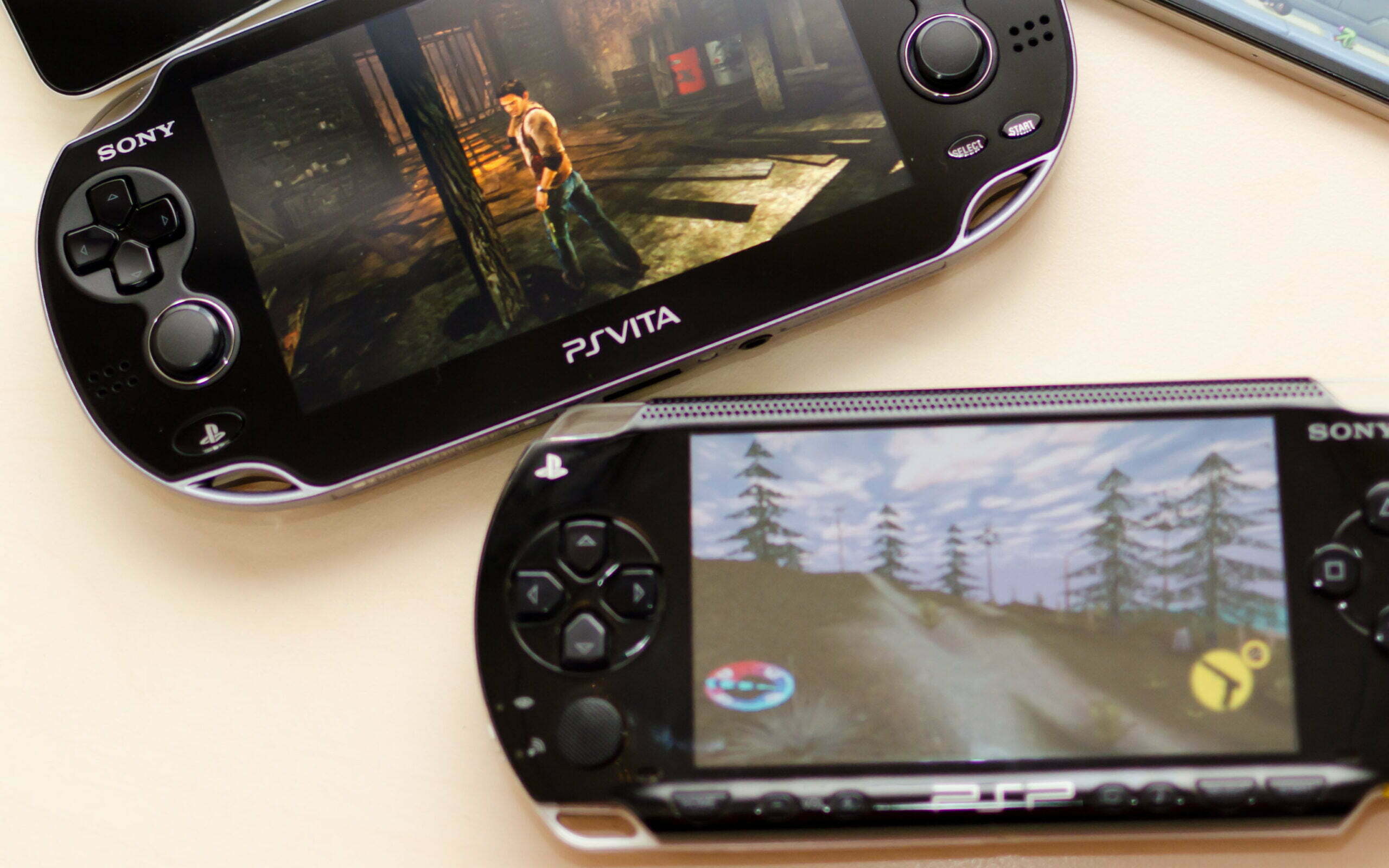 Black PlayStation Vita playing Uncharted: Golden Abyss and a black PlayStation Portable PSP